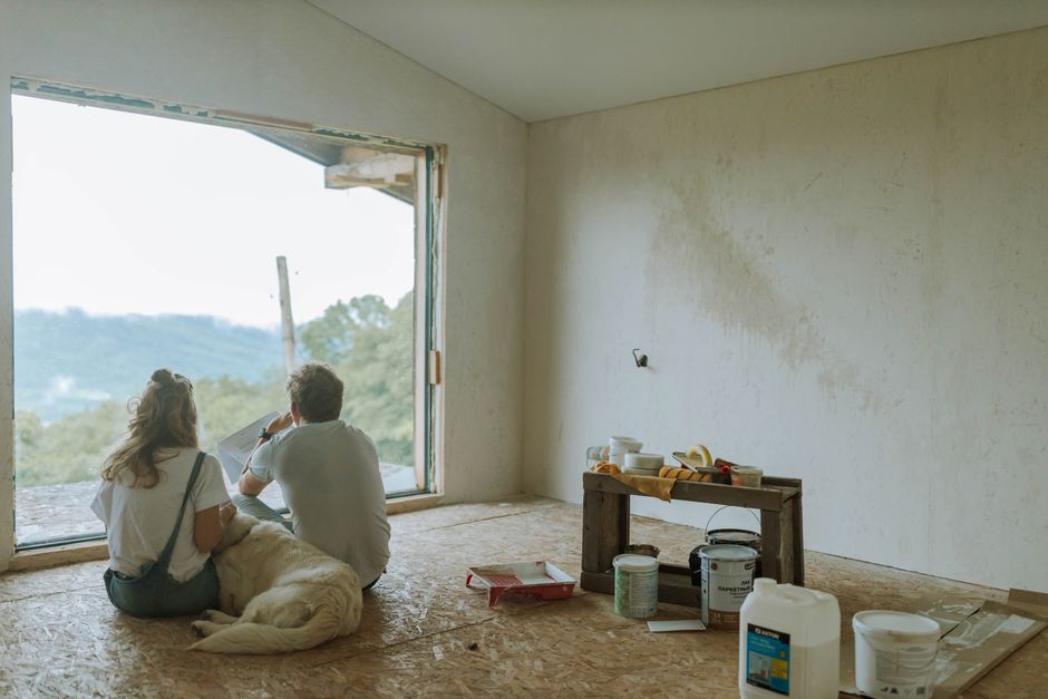 Two homeowners and a contractor reviewing renovation plans in a newly renovated room with large windows